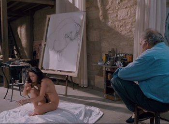 Movie still from “La Belle Noiseuse” (1991), directed by Jacques Rivette – A woman sitting on the ground in front of an easel; Wide shot, High angle
