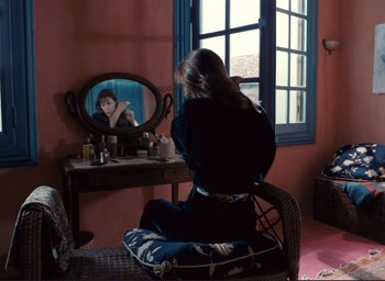Movie still from “La Belle Noiseuse” (1991), directed by Jacques Rivette – A woman sitting in front of a mirror looking at herself in the mirror; Wide shot, Over the shoulder angle