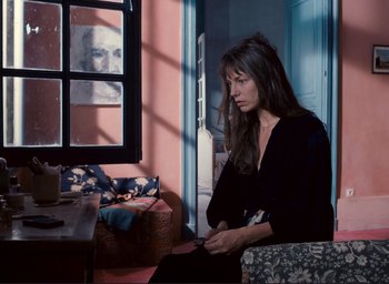 Movie still from “La Belle Noiseuse” (1991), directed by Jacques Rivette – A woman sitting in front of a window holding a cell phone; Medium shot, High angle