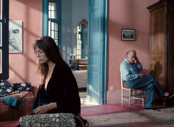 Movie still from “La Belle Noiseuse” (1991), directed by Jacques Rivette – A woman sitting on a chair in front of a man; Wide shot, High angle