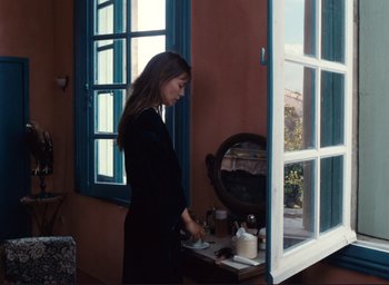 Movie still from “La Belle Noiseuse” (1991), directed by Jacques Rivette – A woman standing in front of a mirror in front of a window; Medium shot, Over the shoulder angle