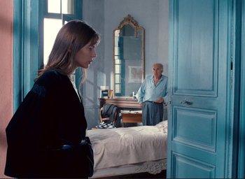 Movie still from “La Belle Noiseuse” (1991), directed by Jacques Rivette – A woman standing in front of a bed in a room; Medium shot, Over the shoulder angle