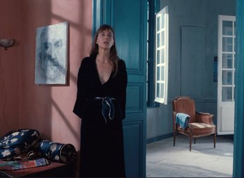 Movie still from “La Belle Noiseuse” (1991), directed by Jacques Rivette – A woman standing in front of a door in a room; Medium shot, Over the shoulder angle