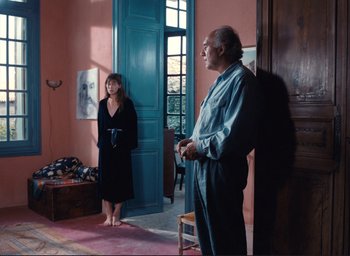 Movie still from “La Belle Noiseuse” (1991), directed by Jacques Rivette – A man and a woman standing in front of a door; Wide shot, Over the shoulder angle
