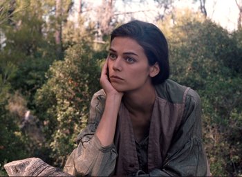 Movie still from “La Belle Noiseuse” (1991), directed by Jacques Rivette – A woman sitting in a field with her head resting on her hand; Close Up shot, High angle