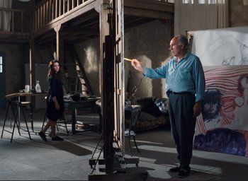 Movie still from “La Belle Noiseuse” (1991), directed by Jacques Rivette – A man and a woman are in a room with a large easel; Wide shot, Low angle