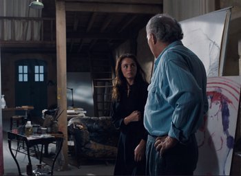 Movie still from “La Belle Noiseuse” (1991), directed by Jacques Rivette – A woman standing next to an older man in a living room; Medium shot, Over the shoulder angle