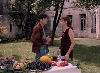 Movie still from “La Belle Noiseuse” (1991), directed by Jacques Rivette – A man and a woman standing next to a table of fruit; Medium shot, Over the shoulder angle