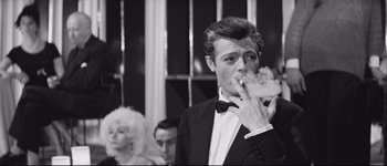 Movie still from “La Dolce Vita” (1960), directed by Federico Fellini – A black and white photo of a man in a tuxedo eating a piece of cake; Medium shot, Low angle