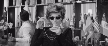 Movie still from “La Dolce Vita” (1960), directed by Federico Fellini – A woman in a black dress holding a purse and smoking a cigarette; Medium shot, Low angle