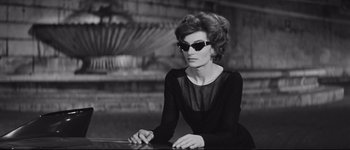 Movie still from “La Dolce Vita” (1960), directed by Federico Fellini – A woman in a black dress wearing sunglasses; Medium shot, Low angle