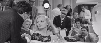 Movie still from “La Dolce Vita” (1960), directed by Federico Fellini – A black - and - white photo of a woman sitting at a table; Medium shot, Over the shoulder angle