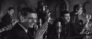 Movie still from “La Dolce Vita” (1960), directed by Federico Fellini – A man with his hands up in front of microphones; Close Up shot, Over the shoulder angle