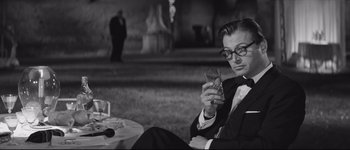 Movie still from “La Dolce Vita” (1960), directed by Federico Fellini – A black and white photo of a man holding a drink; Medium shot, Over the shoulder angle