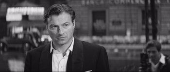Movie still from “La Dolce Vita” (1960), directed by Federico Fellini – Black and white photograph of a man wearing a suit; Close Up shot, Over the shoulder angle