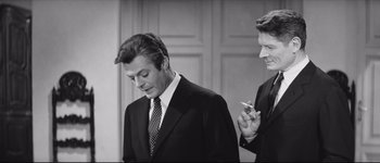 Movie still from “La Dolce Vita” (1960), directed by Federico Fellini – A man in a suit and tie standing next to another man in a suit and tie; Medium shot, Over the shoulder angle