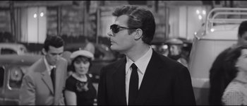 Movie still from “La Dolce Vita” (1960), directed by Federico Fellini – A man in a suit and sunglasses looking to his left; Close Up shot, Over the shoulder angle