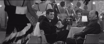 Movie still from “La Dolce Vita” (1960), directed by Federico Fellini – A black and white photo of a man sitting at a table; Medium shot, Over the shoulder angle