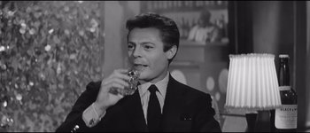 Movie still from “La Dolce Vita” (1960), directed by Federico Fellini – A black and white photo of a man in a suit drinking a glass of wine; Close Up shot, Over the shoulder angle