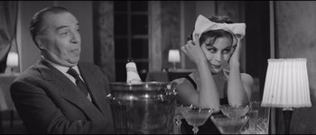 Movie still from “La Dolce Vita” (1960), directed by Federico Fellini – A woman sitting at a table with a glass of wine; Medium shot, Over the shoulder angle