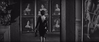 Movie still from “La Dolce Vita” (1960), directed by Federico Fellini – A woman in a black dress walking in front of a wall of paintings; Medium shot, Over the shoulder angle