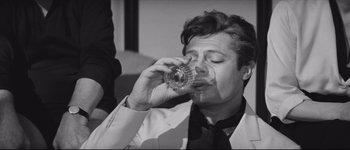 Movie still from “La Dolce Vita” (1960), directed by Federico Fellini – A man in a white jacket drinking a glass of water; Close Up shot, High angle
