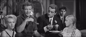 Movie still from “La Dolce Vita” (1960), directed by Federico Fellini – Three men sitting at a dinner table eating pasta; Medium shot, Over the shoulder angle