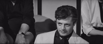 Movie still from “La Dolce Vita” (1960), directed by Federico Fellini – A black and white photo of a man wearing a suit; Close Up shot, Over the shoulder angle