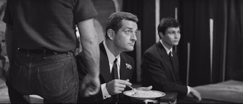 Movie still from “La Dolce Vita” (1960), directed by Federico Fellini – A black and white photo of a man eating a plate of food; Medium shot, High angle