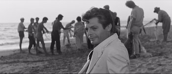 Movie still from “La Dolce Vita” (1960), directed by Federico Fellini – A black and white photo of a man on the beach; Close Up shot, Over the shoulder angle
