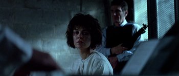 Movie still from “Nikita” (1990), directed by Luc Besson – A man and a woman are in a dark room; Medium shot, Over the shoulder angle