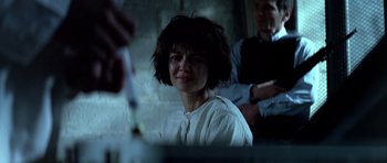 Movie still from “Nikita” (1990), directed by Luc Besson – A woman in a white shirt is sitting in front of a brick wall; Close Up shot, Over the shoulder angle