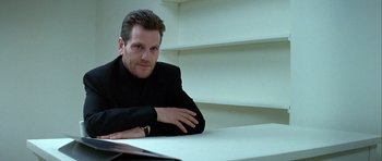 Movie still from “Nikita” (1990), directed by Luc Besson – A man sitting at a table with his arms crossed; Close Up shot, Low angle