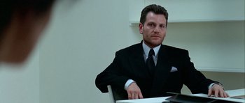 Movie still from “Nikita” (1990), directed by Luc Besson – A man sitting at a table wearing a suit and tie; Close Up shot, Low angle