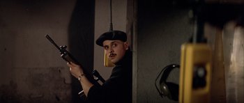 Movie still from “Nikita” (1990), directed by Luc Besson – A man holding a gun in a room with headphones hanging from the side of the wall; Close Up shot, Low angle
