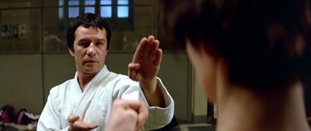 Movie still from “Nikita” (1990), directed by Luc Besson – A man in a white shirt is practicing karate; Close Up shot, Over the shoulder angle
