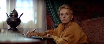 Movie still from “Nikita” (1990), directed by Luc Besson – An older woman sitting at a table writing on a paper; Medium shot, Low angle