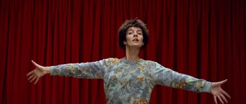 Movie still from “Nikita” (1990), directed by Luc Besson – A person standing in front of a red curtain with their arms outstretched; Medium shot, Overhead angle