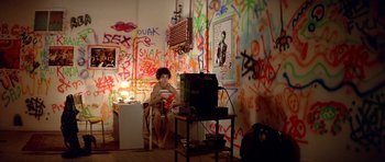 Movie still from “Nikita” (1990), directed by Luc Besson – A person sitting in front of a tv in a room with graffiti on the walls; Wide shot, High angle