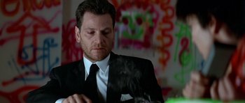 Movie still from “Nikita” (1990), directed by Luc Besson – A man wearing a suit and tie smoking a cigarette; Close Up shot, Low angle