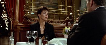 Movie still from “Nikita” (1990), directed by Luc Besson – A woman sitting at a table in front of a glass of wine; Medium shot, Over the shoulder angle
