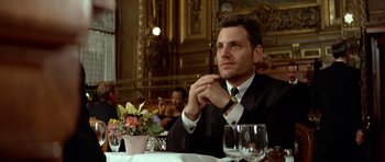 Movie still from “Nikita” (1990), directed by Luc Besson – A man sitting at a table with a glass of wine in front of him; Medium shot, Low angle