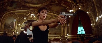 Movie still from “Nikita” (1990), directed by Luc Besson – A woman holding a gun in a room with ornate ceilings; Medium shot, Low angle