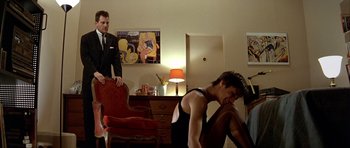 Movie still from “Nikita” (1990), directed by Luc Besson – A man sitting on a chair in front of another man in a suit; Wide shot, Over the shoulder angle