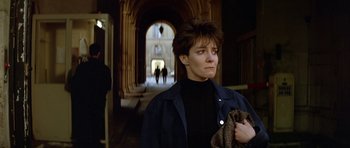Movie still from “Nikita” (1990), directed by Luc Besson – A woman in a black jacket standing in front of an archway; Medium shot, Low angle