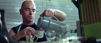 Movie still from “Nikita” (1990), directed by Luc Besson – A man pouring a cup of coffee into a mug; Medium shot, Low angle