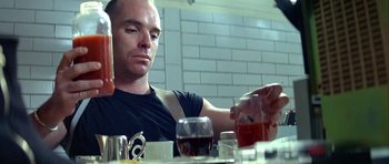 Movie still from “Nikita” (1990), directed by Luc Besson – A man sitting at a table with a drink in front of him; Close Up shot, Low angle