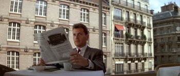 Movie still from “Nikita” (1990), directed by Luc Besson – A man sitting at a table reading a newspaper; Medium shot, Low angle