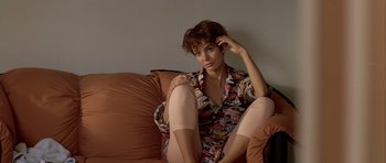 Movie still from “Nikita” (1990), directed by Luc Besson – A woman sitting on a couch with her hands on her head; Medium shot, High angle