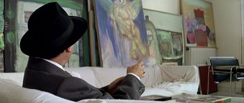 Movie still from “Nikita” (1990), directed by Luc Besson – A man sitting in front of a painting of an angel; Close Up shot, Over the shoulder angle